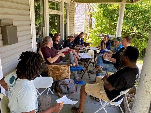 A group of students and faculty sitting on a porch having a discussion.