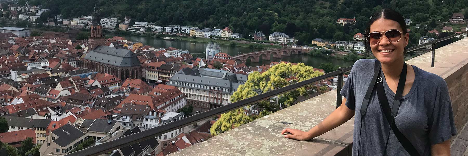 A student leans on a wall overlooking a European city.